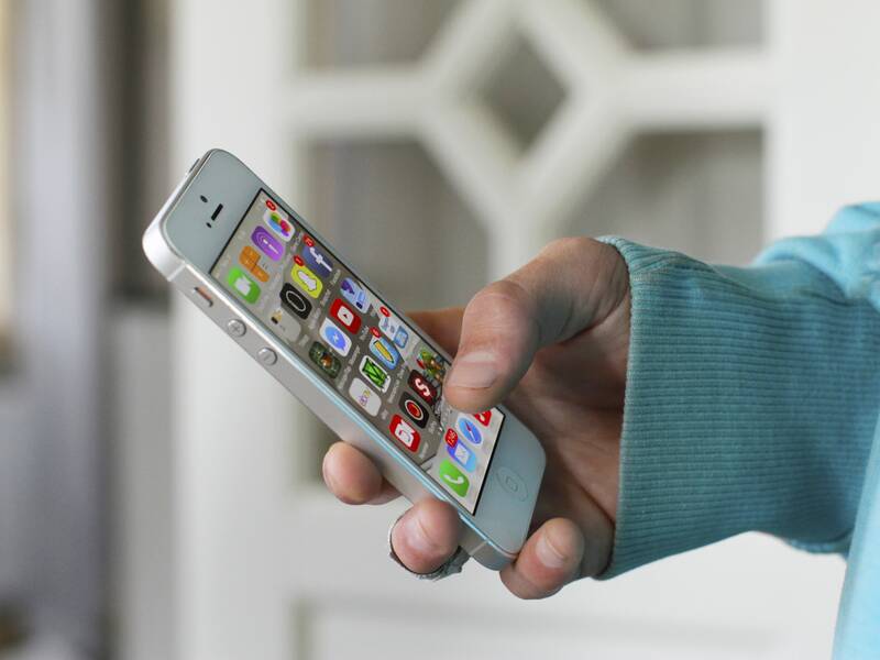 Eine Person hält ein Smartphone in einer Hand, auf dessen Bildschirm bunte App-Symbole zu sehen sind.