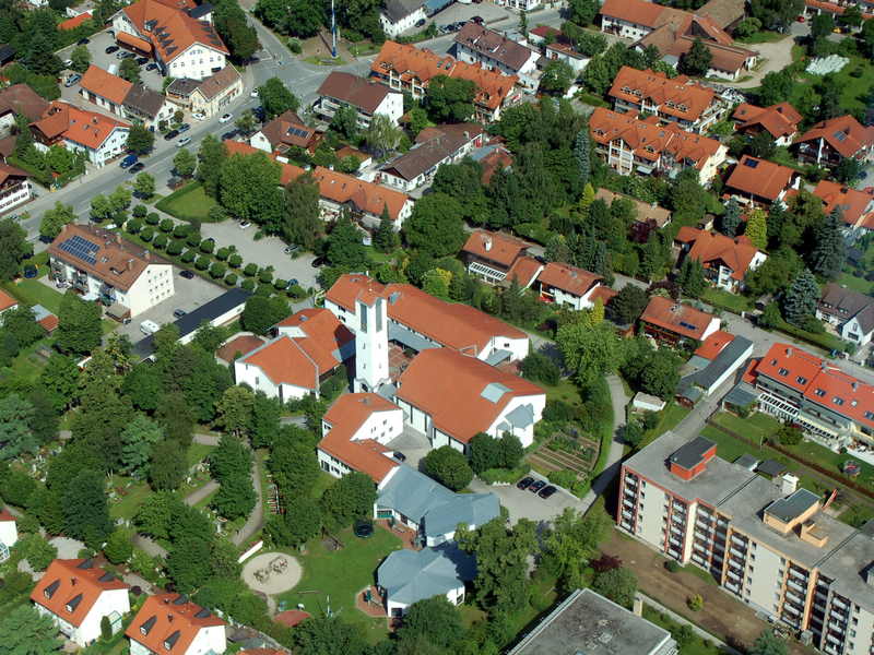 Luftaufnahme einer grünen Wohngegend mit vielen roten Ziegeldächern und einem markanten weißen Turm in der Mitte.